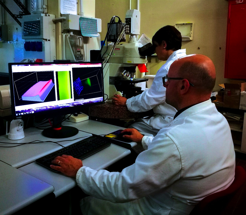 Laboratorio Micro e Nanostrutture per la Fotonica - Lettura di innovativi rivelatori di radiazione mediante microscopio ottico in fluorescenza. Sotto l'obiettivo del microscopio è visibile l'emissione di luce del rivelatore e sullo schermo è ricostruita la curva di Bragg acquisita